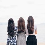 three woman looking back and facing body of water