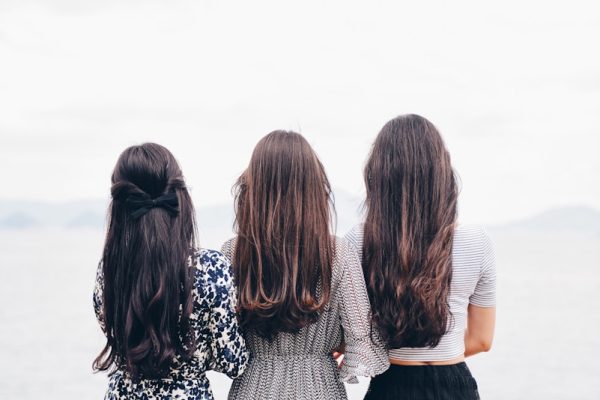 three woman looking back and facing body of water